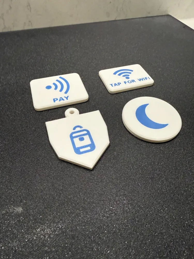 Four printed NFC tags on a bench: a Pay tag, a Tap-for-Wi-Fi tag, a kids bag tag and a sleep-mode disc